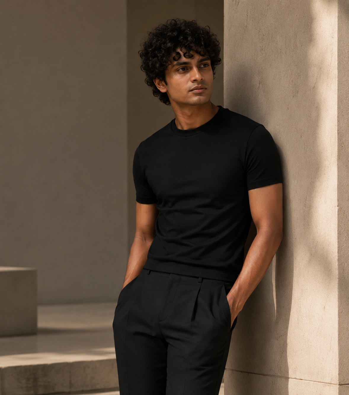 Model in a black tee and trousers leaning against a stone wall